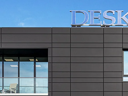 Moderno edificio de oficinas DESKO con fachada metálica oscura, grandes ventanales y logotipo de la empresa en el tejado.