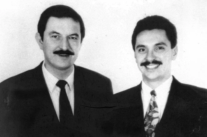 Fotograf&iacute;a en blanco y negro de dos hombres con traje y corbata, ambos con bigote, retratados de frente sobre un fondo claro.