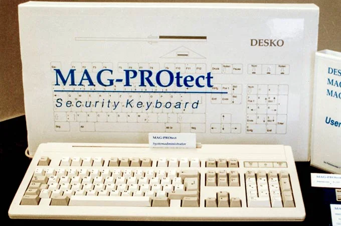 Foto de producto de un teclado de seguridad DESKO "MAG-PROtect" beige con embalaje y manual de usuario al fondo.
