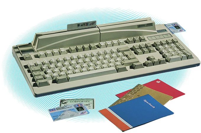 Teclado de seguridad DESKO beige con lector de tarjetas integrado, con tarjetas de identidad y de cr&eacute;dito sobre fondo claro.