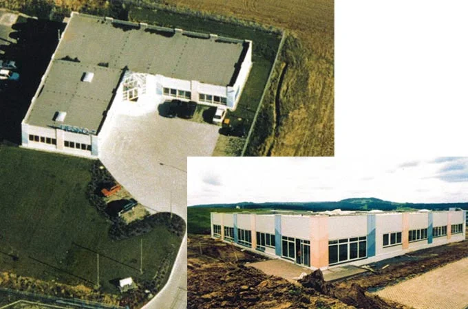 Vista a&eacute;rea hist&oacute;rica y vista exterior de un antiguo edificio de la empresa DESKO en un entorno rural durante la fase de construcci&oacute;n.