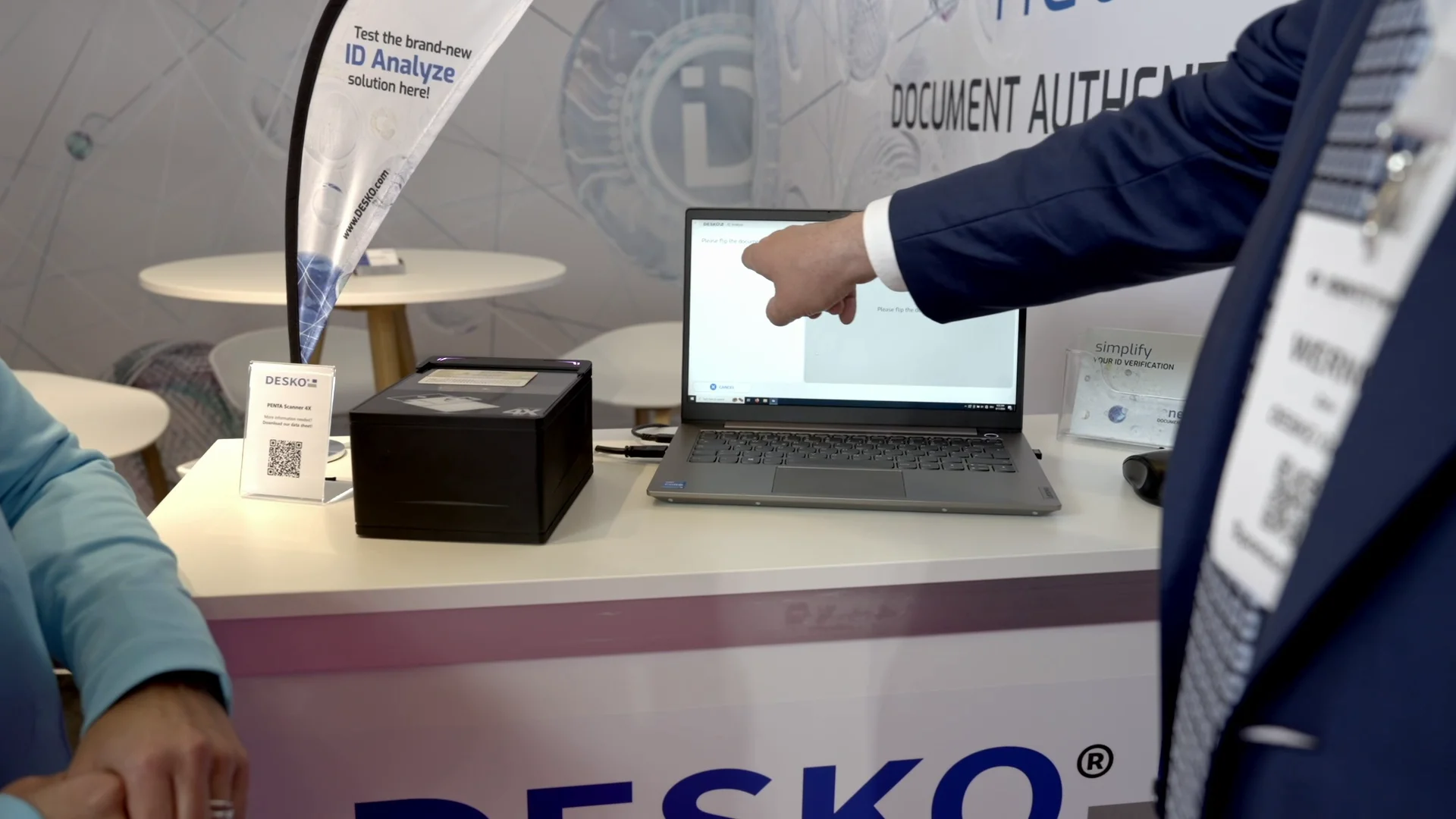 Un hombre se&ntilde;ala un ordenador port&aacute;til con datos de identificaci&oacute;n, junto al esc&aacute;ner de documentos del puesto de verificaci&oacute;n de identidad.
