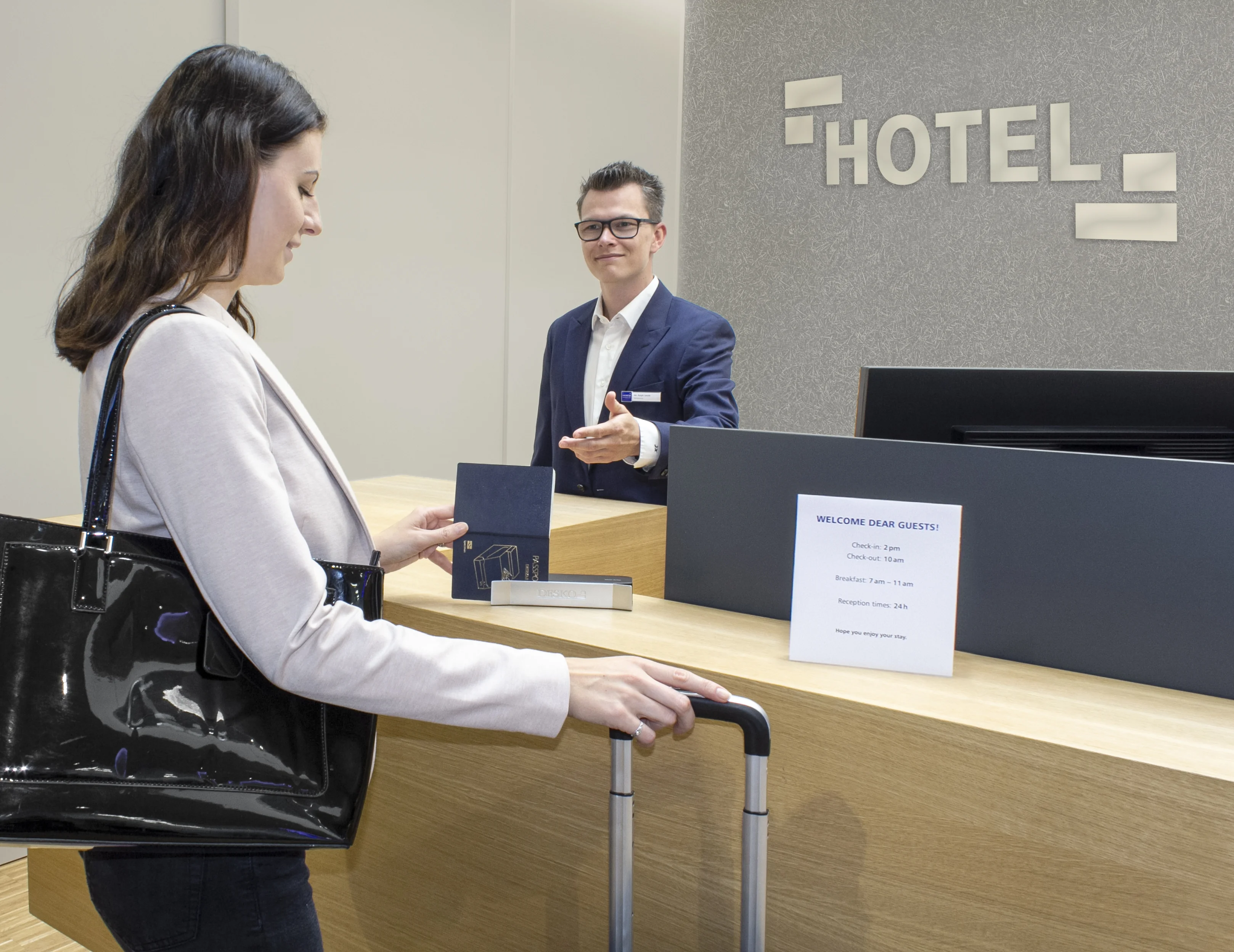 Recepci&oacute;n del hotel con el hu&eacute;sped en el momento del check-in, entregando una tarjeta de identificaci&oacute;n en el mostrador mientras el empleado la toma.