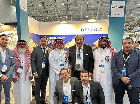 Un grupo internacional de visitantes de la feria y empleados de DESKO juntos en el stand de DESKO para soluciones de identidad.