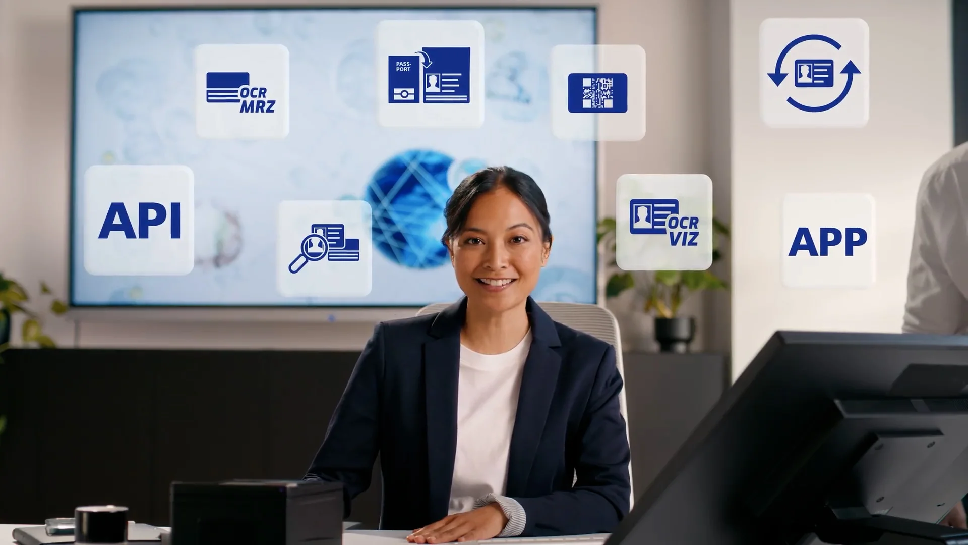 Mujer sentada en un escritorio frente a una pantalla, rodeada de iconos flotantes de API, aplicaci&oacute;n, OCR, pasaporte y comprobaci&oacute;n del DNI.
