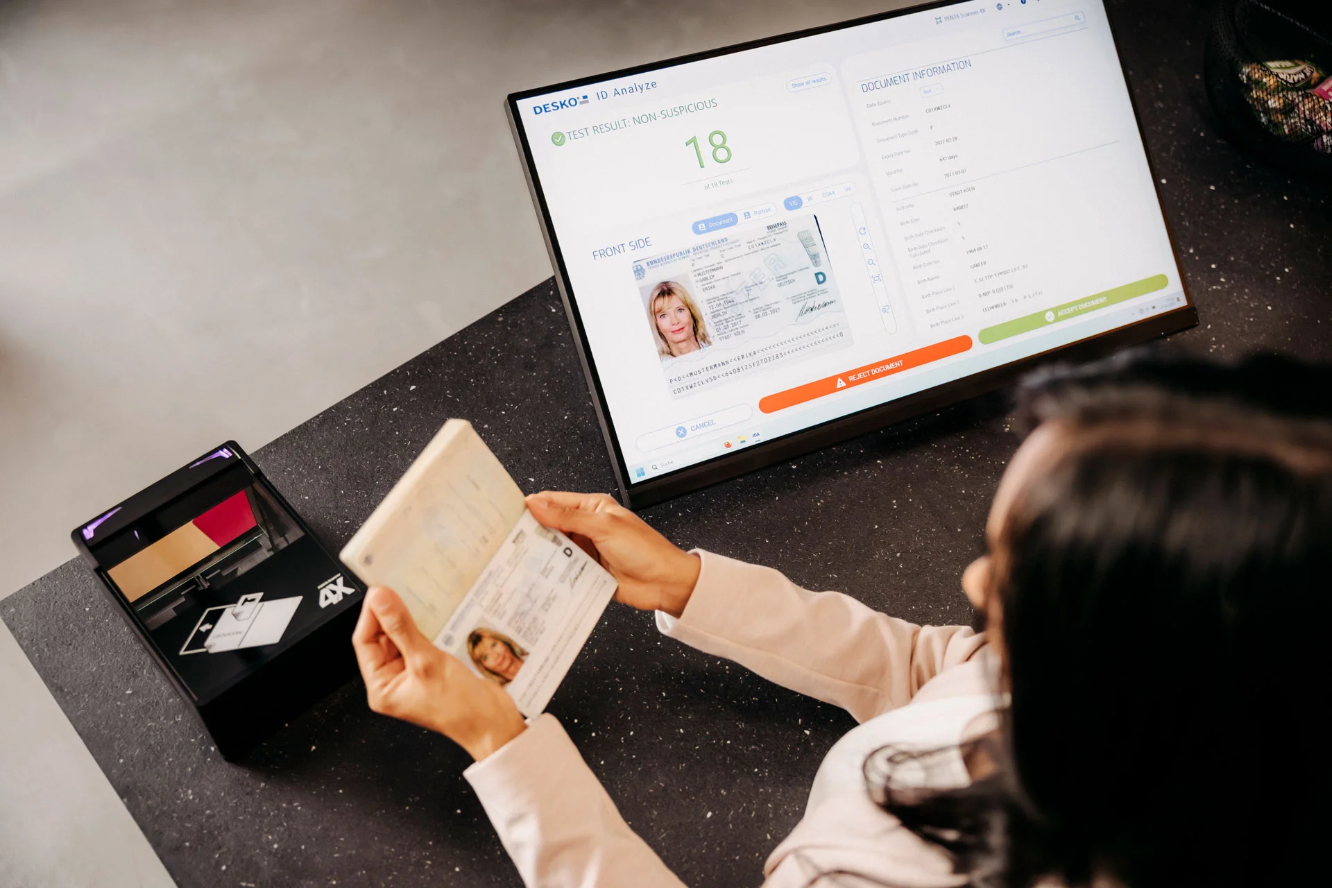 Una persona sostiene un pasaporte abierto delante de un dispositivo de comprobaci&oacute;n, mientras en una pantalla se muestra el an&aacute;lisis digital del DNI con el resultado de la comprobaci&oacute;n.
