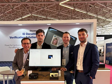 Cuatro hombres están de pie detrás de un monitor en un stand de una feria.