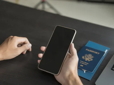 Mobiltelefon in der Hand, Ausweisdokumente auf dem Tisch