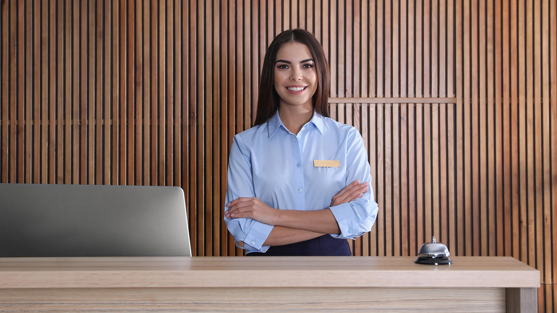 Eine Hotelmitarbeiterin steht mit verschr&auml;nkten Armen an der Rezeption vor einem Monitor.