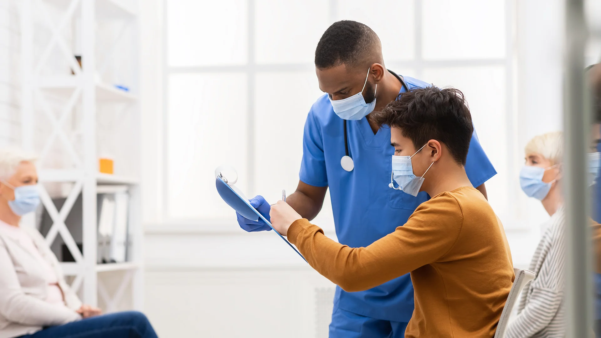 Ein junger Patient mit Mundschutz unterschreibt ein Dokument in einer medizinischen Einrichtung.