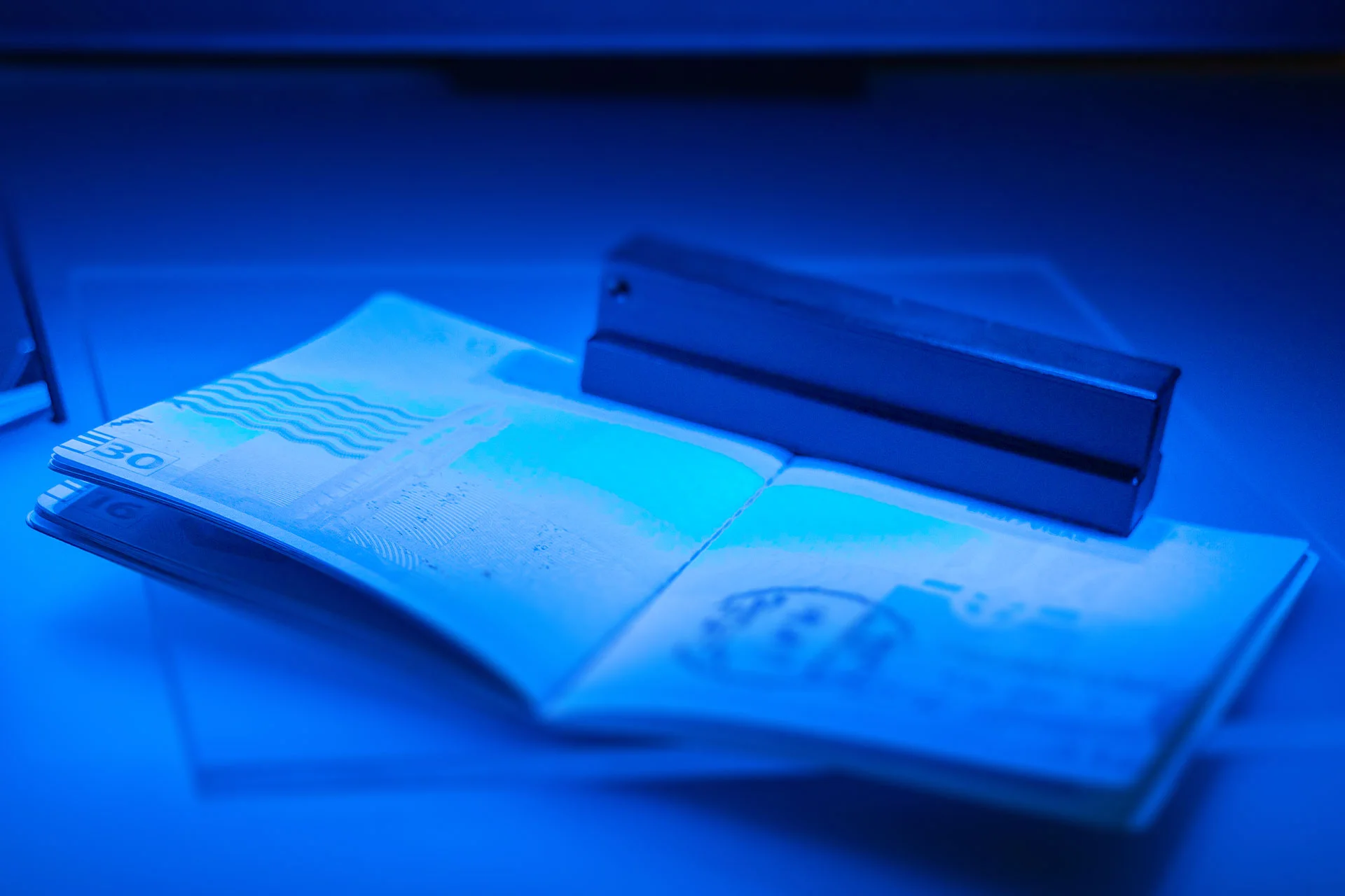 Un pasaporte abierto se coloca bajo una luz azul ultravioleta en un esc&aacute;ner de documentos para realizar un control de seguridad.