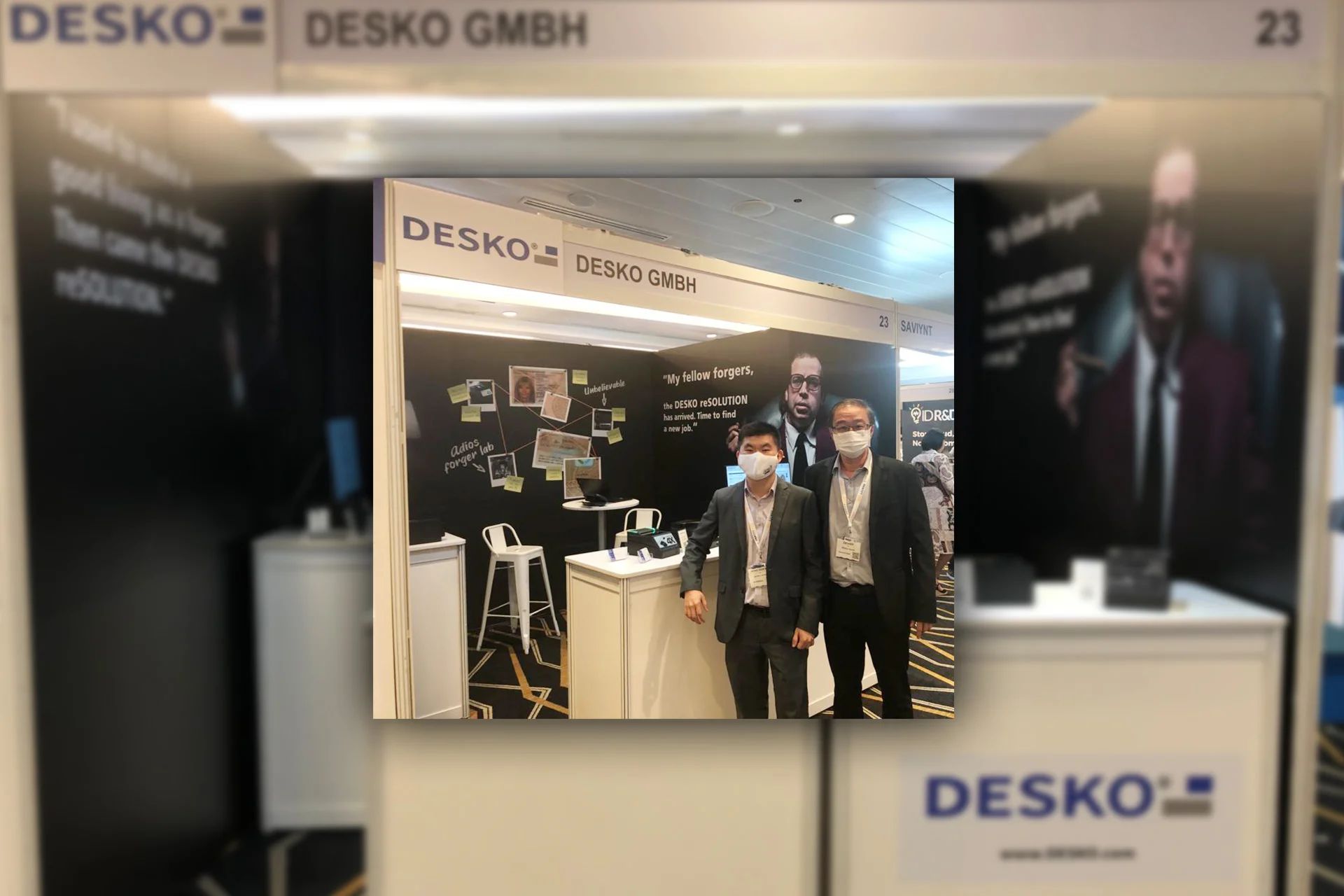 DESKO Messestand auf der Identity Week Asia 2022 in Singapur mit zwei Mitarbeitern vor der Produktpr&auml;sentation zur Dokumentenpr&uuml;fung.