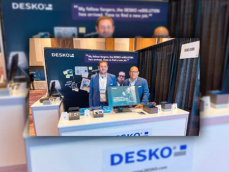 Dos empleados de DESKO en el stand de la feria con el motivo reSOLUTION, la presentación del escáner 4X y la marca al fondo.