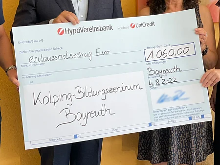 Varias personas sostienen un gran cheque donativo de 1.060 euros para el Centro de Educación Kolping de Bayreuth.