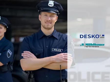 Dos policías uniformados con los brazos cruzados, un agente en primer plano, logotipos de DESKO y Mühlbauer junto a ellos.