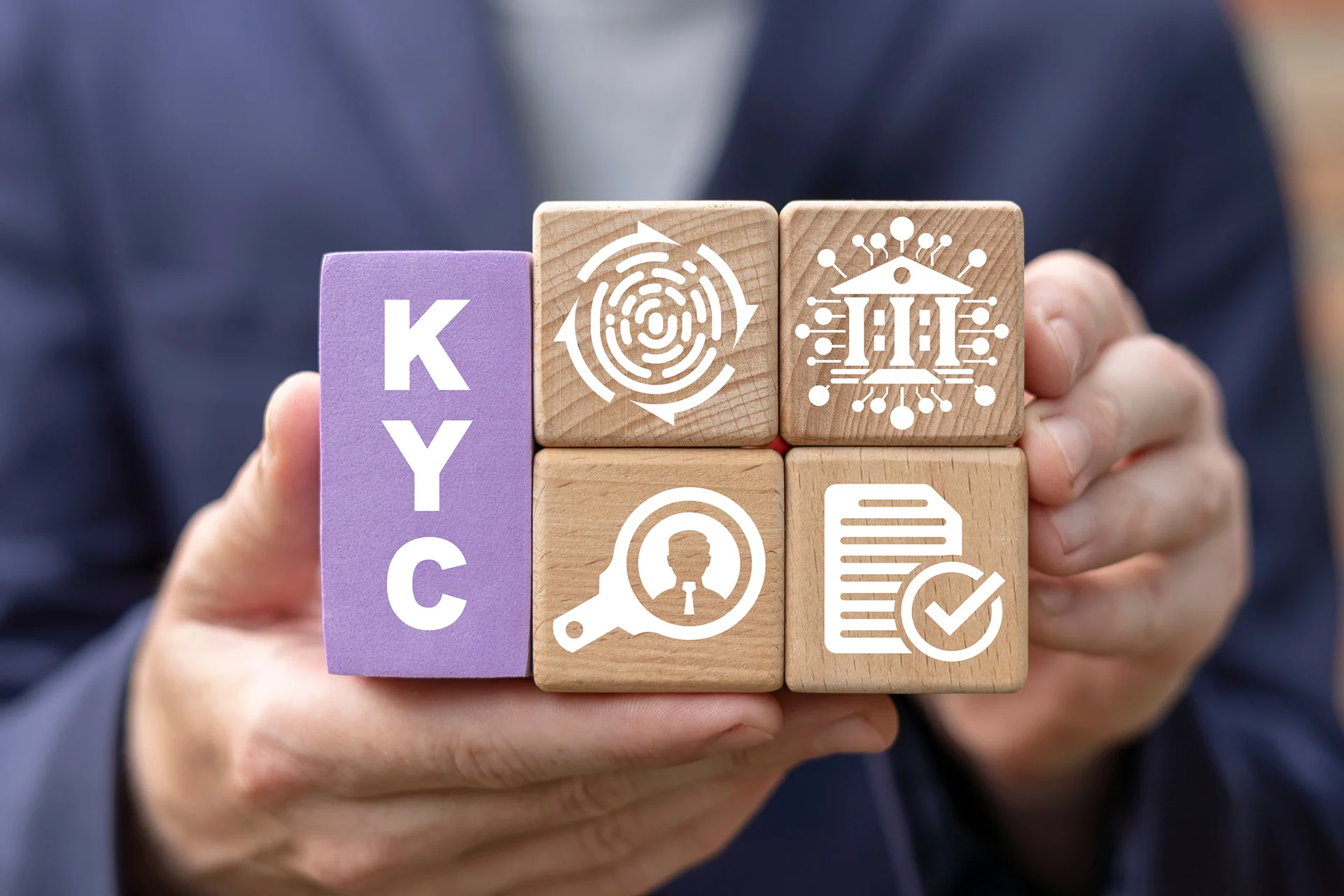 Manos sujetando bloques de madera con letras y s&iacute;mbolos KYC para comprobaci&oacute;n de identidad, banco, documentos y auditor&iacute;a.